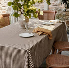 a table set for a meal, with a checkered tablecloth, plates, glasses, and a vase of leaves. The table is surrounded by chairs, creating a cozy dining atmosphere.