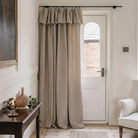 a cozy corner of a room with a wooden table, a white armchair, and a striped curtain covering a doorway.
