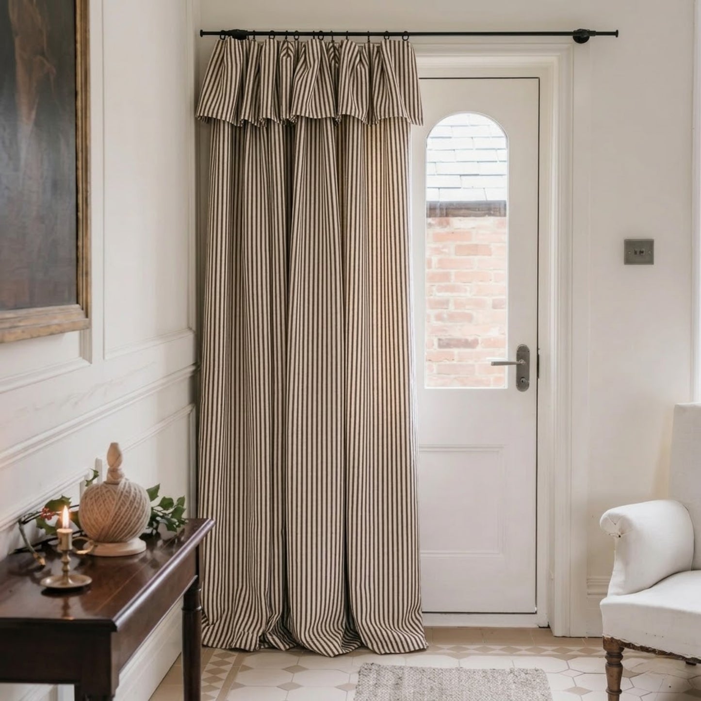 a cozy corner of a room with a wooden table, a white armchair, and a striped curtain covering a doorway.